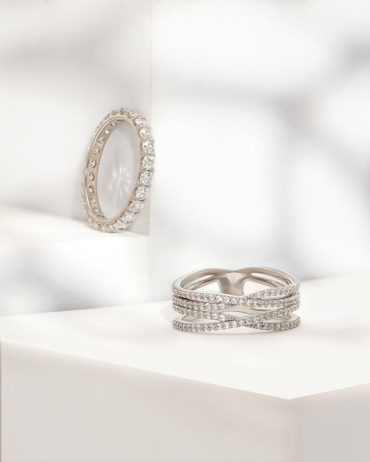 Four row round pave lab grown diamond wedding band in white gold beside a full eternity band on a white plinth