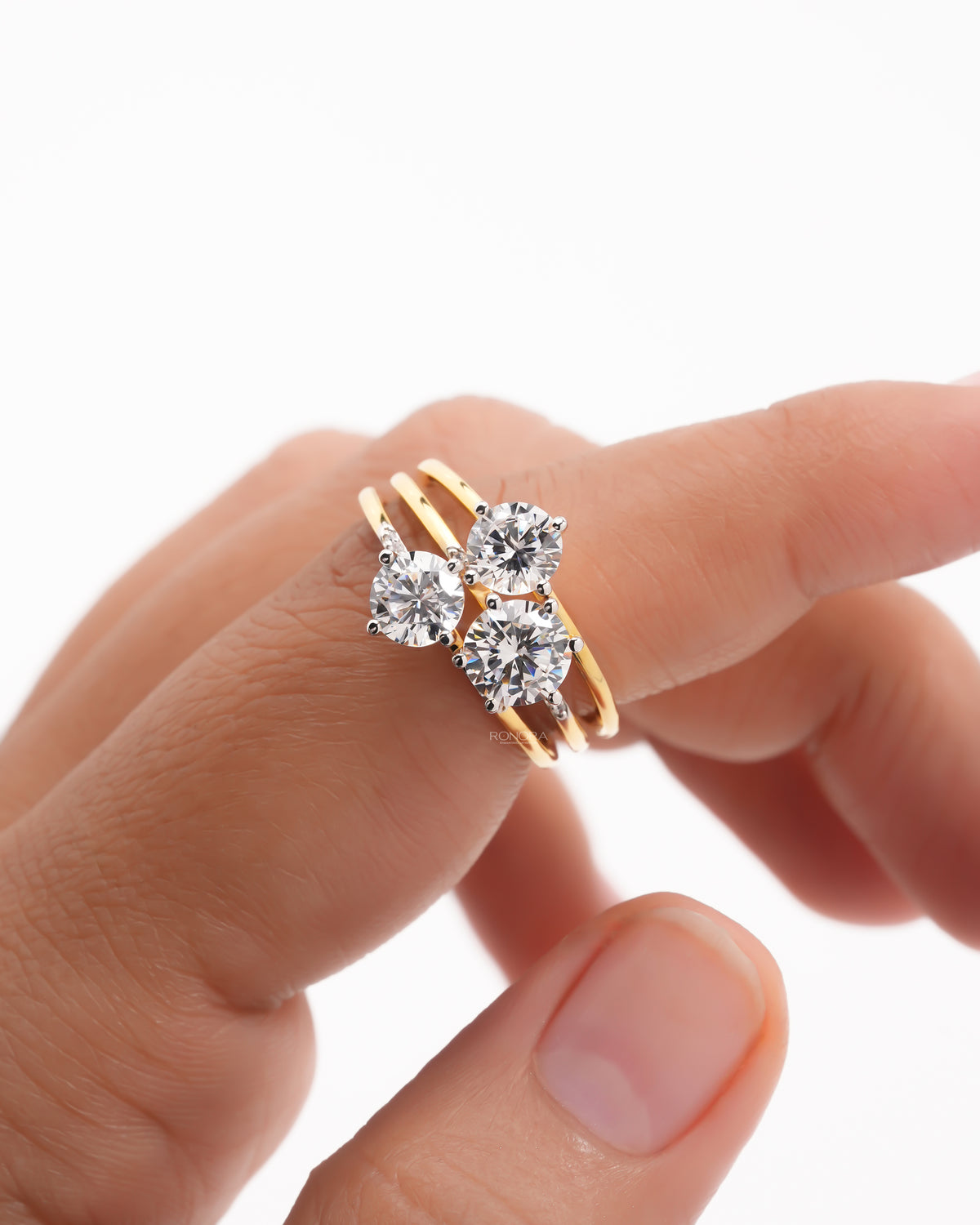 Close-up of a round three stone lab grown diamond cluster ring in yellow gold held on a fingertip, split band
