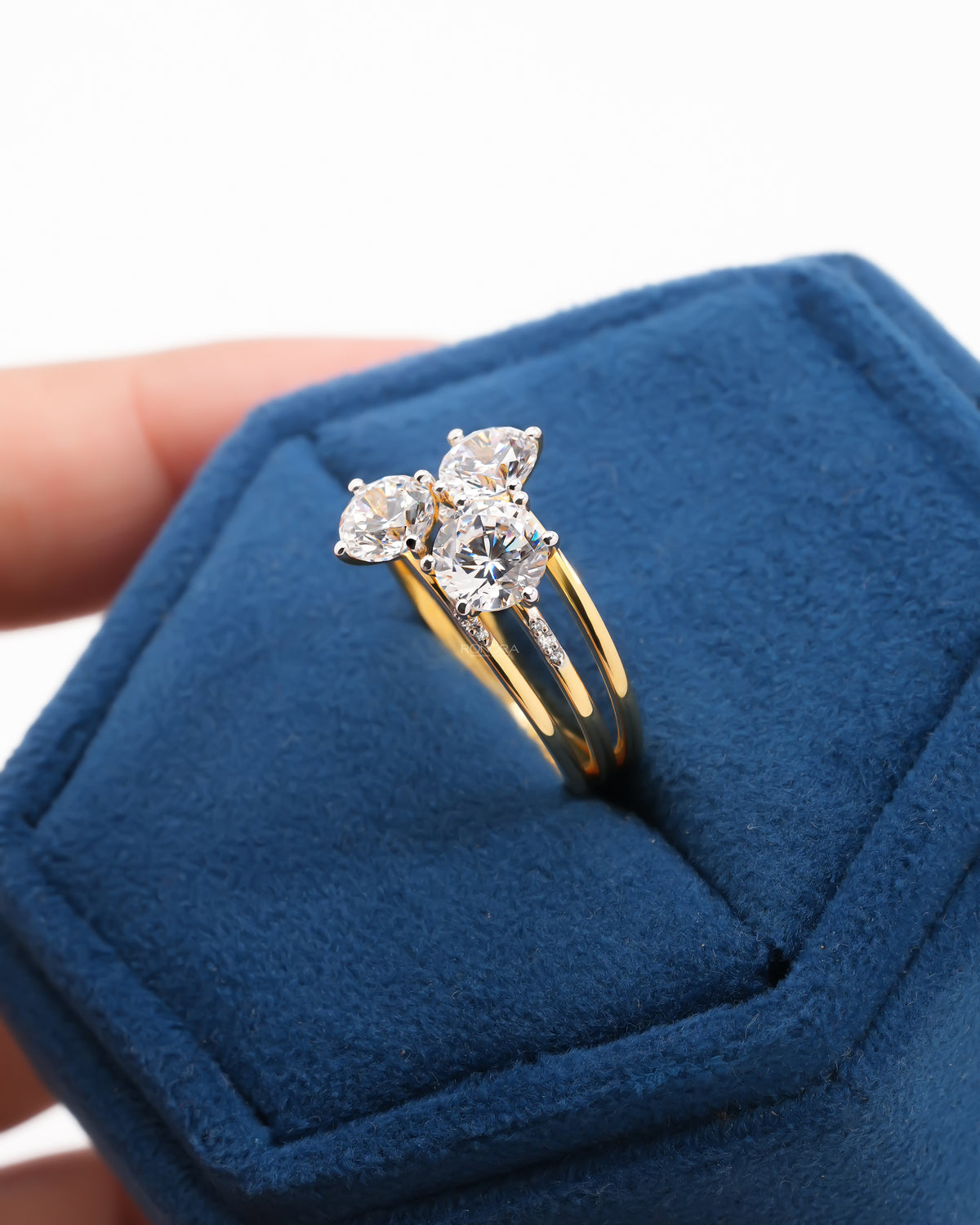 Round three stone lab grown diamond cluster ring in yellow gold sitting in a blue velvet ring box, angled view