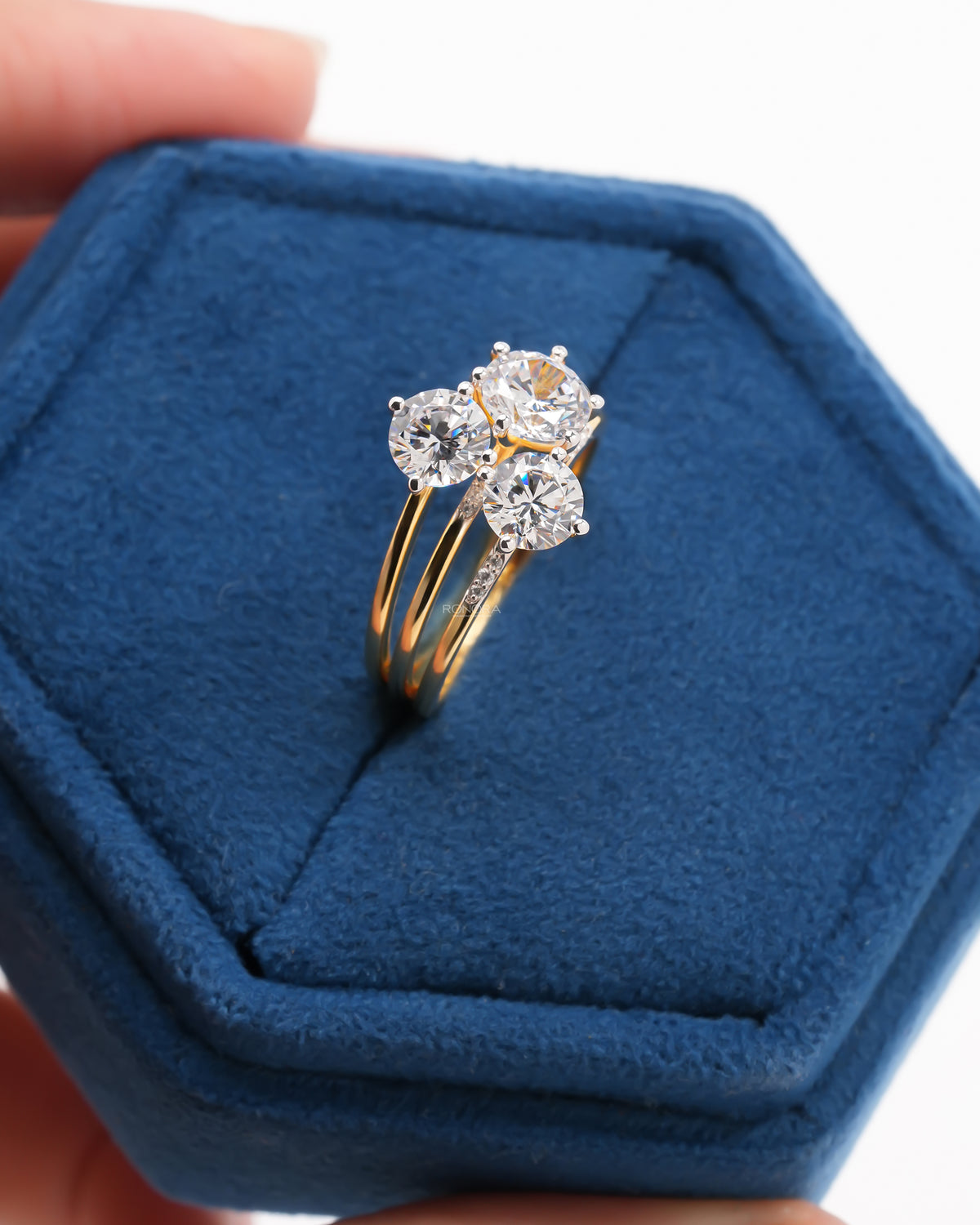 Round three stone lab grown diamond cluster ring in yellow gold, held in a blue velvet hexagon ring box
