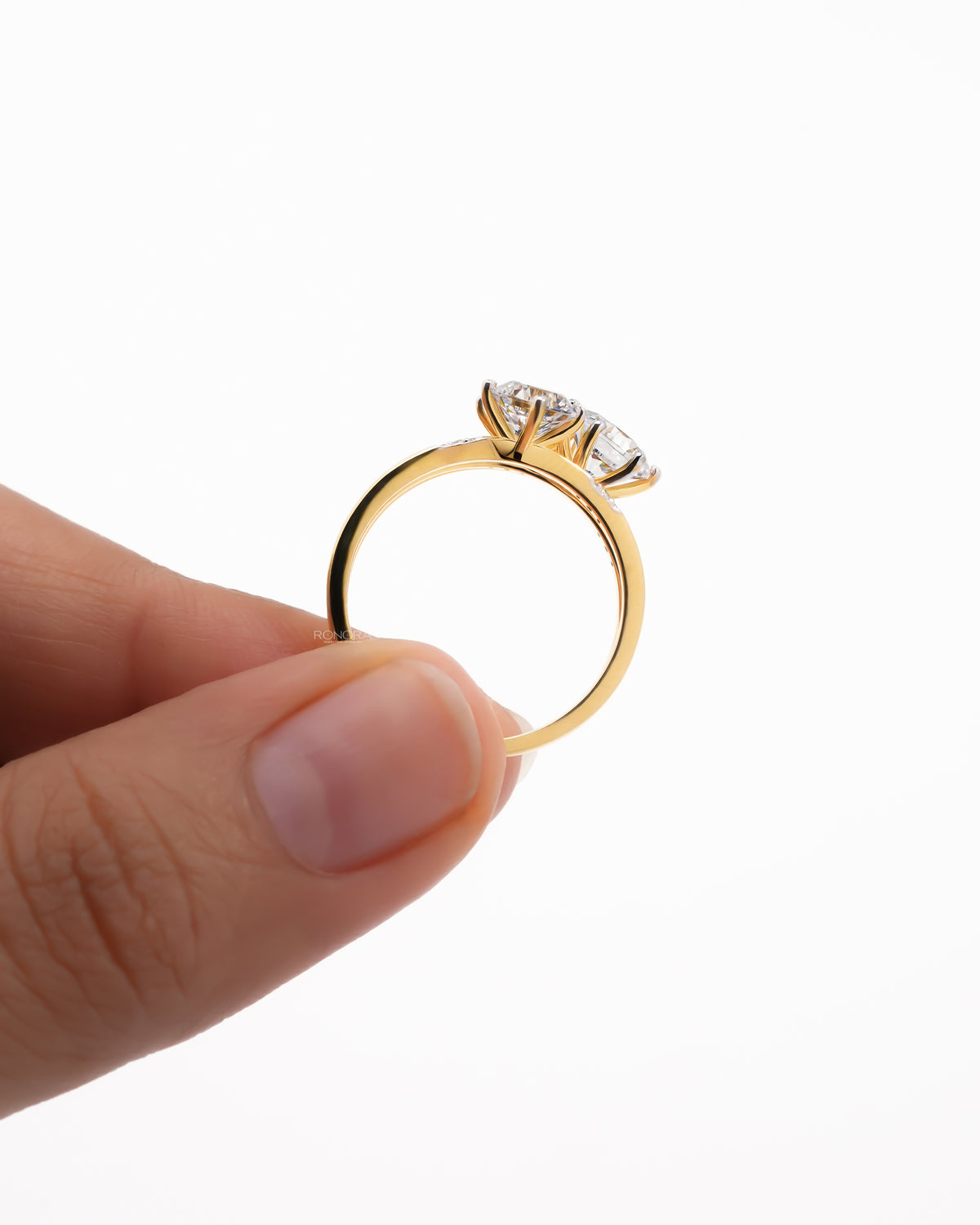 Side profile of a yellow gold round three stone lab grown diamond cluster ring held between two fingers