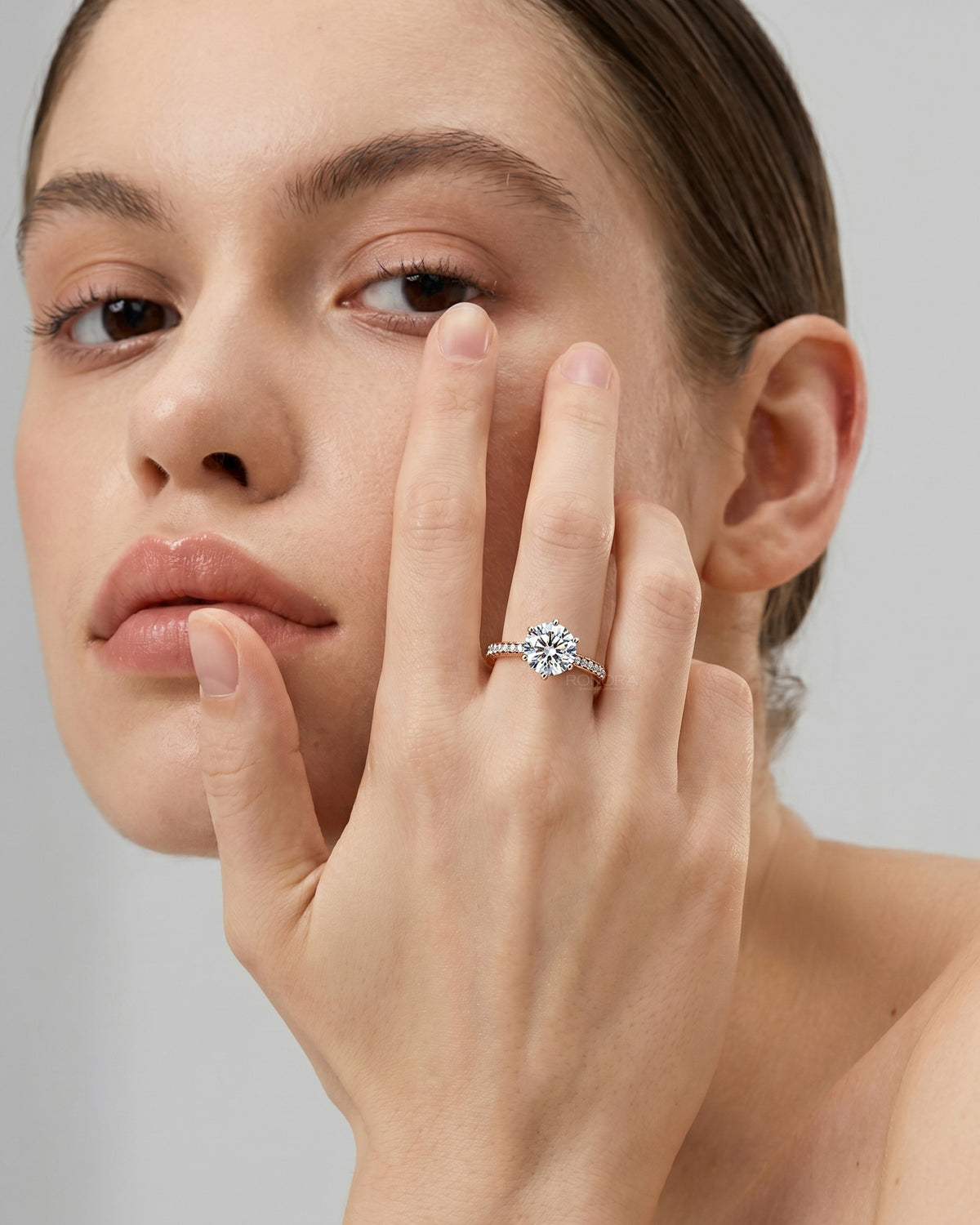 Model wearing a round moissanite pave ring with a sparkling centre stone, hand held against her cheek