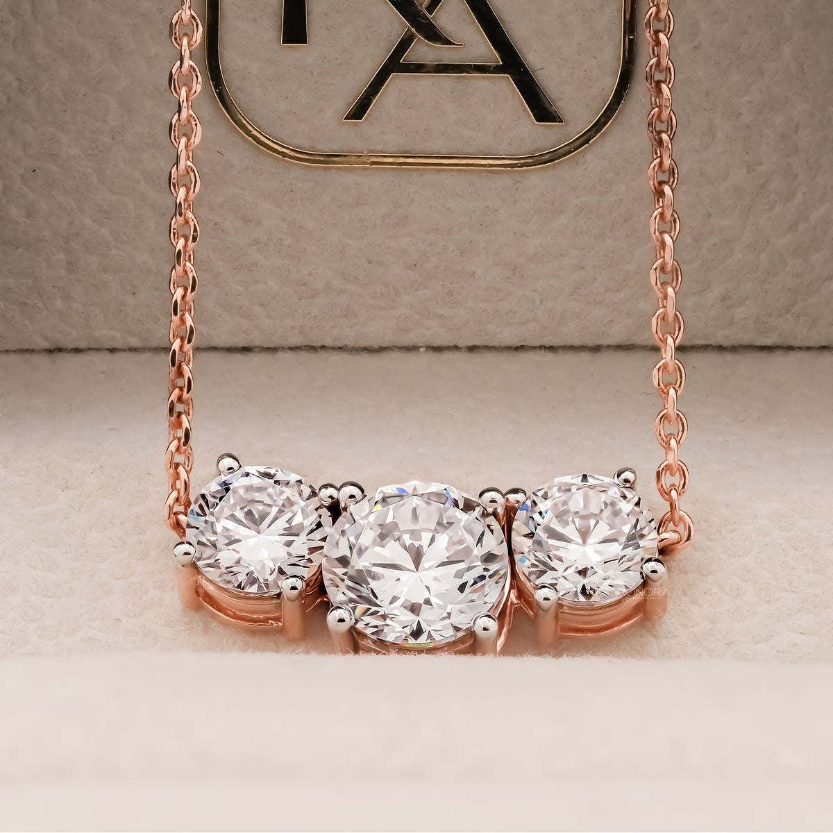 Close-up of a rose gold three stone round lab grown diamond necklace in a beige velvet jewelry box