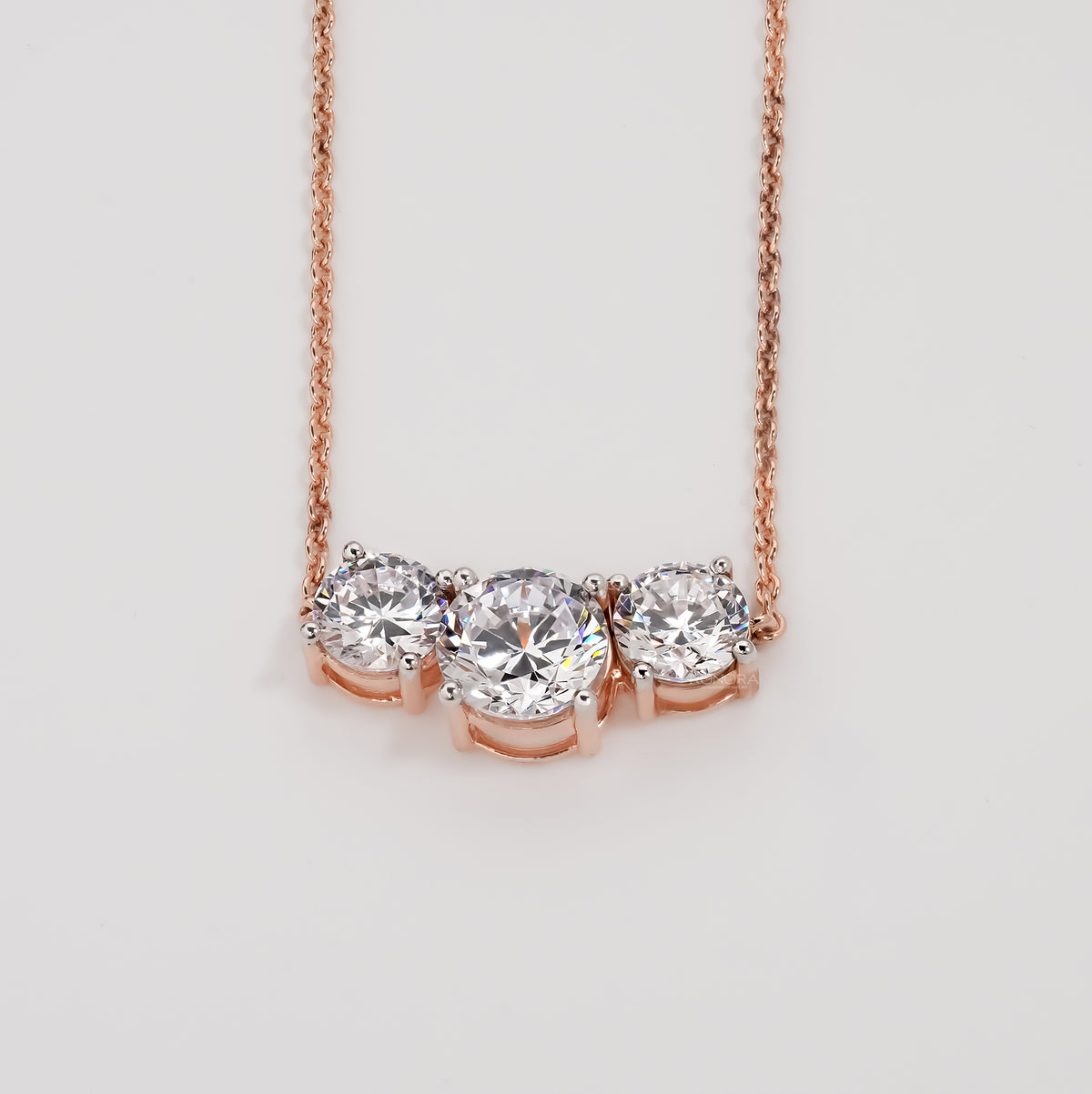 Three stone round lab grown diamond necklace in rose gold on a plain light grey background, front view