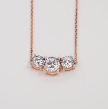 Three stone round lab grown diamond necklace in rose gold on a plain light grey background, front view