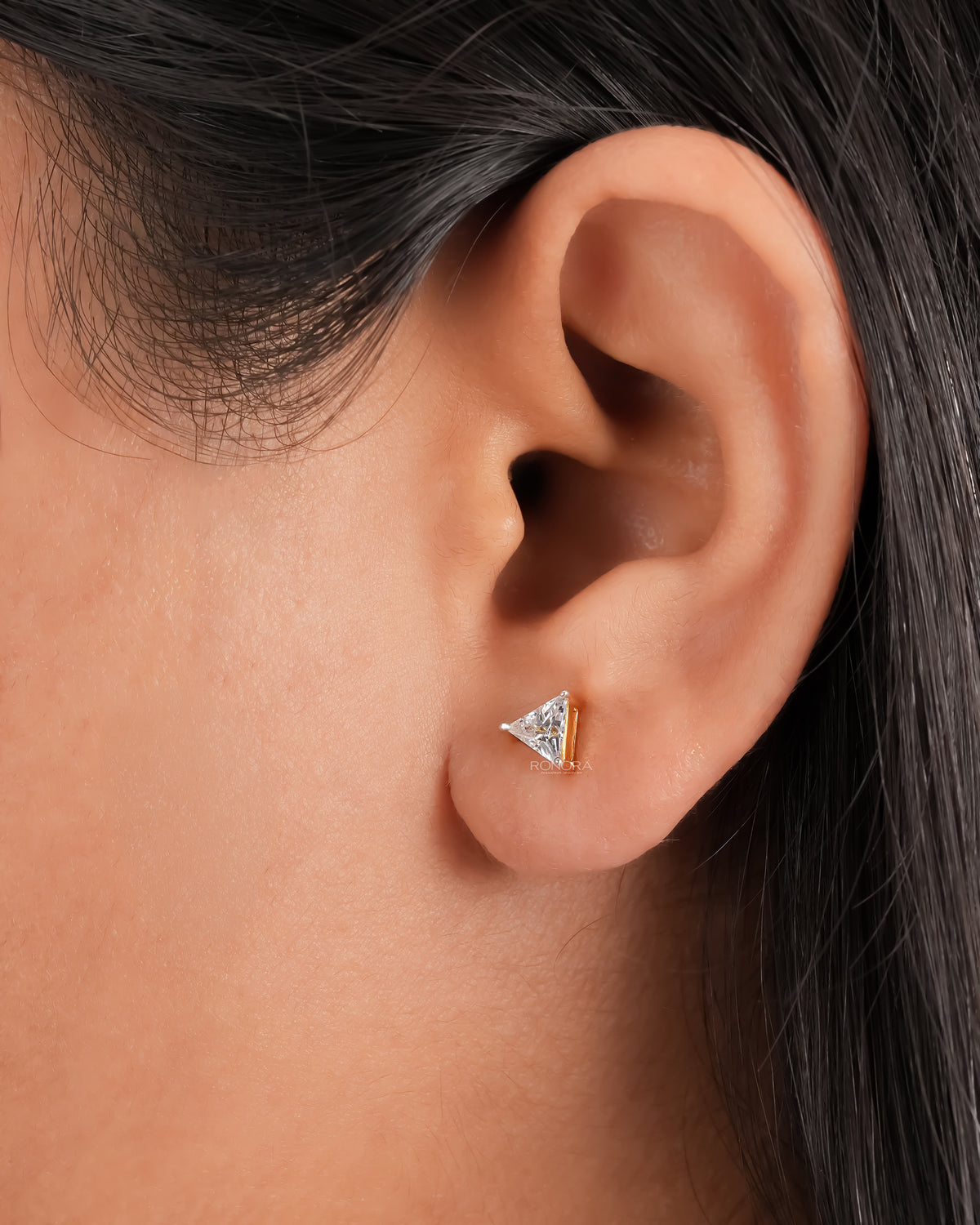 Trillion cut lab grown diamond stud earring in yellow gold worn on a woman's ear, close-up