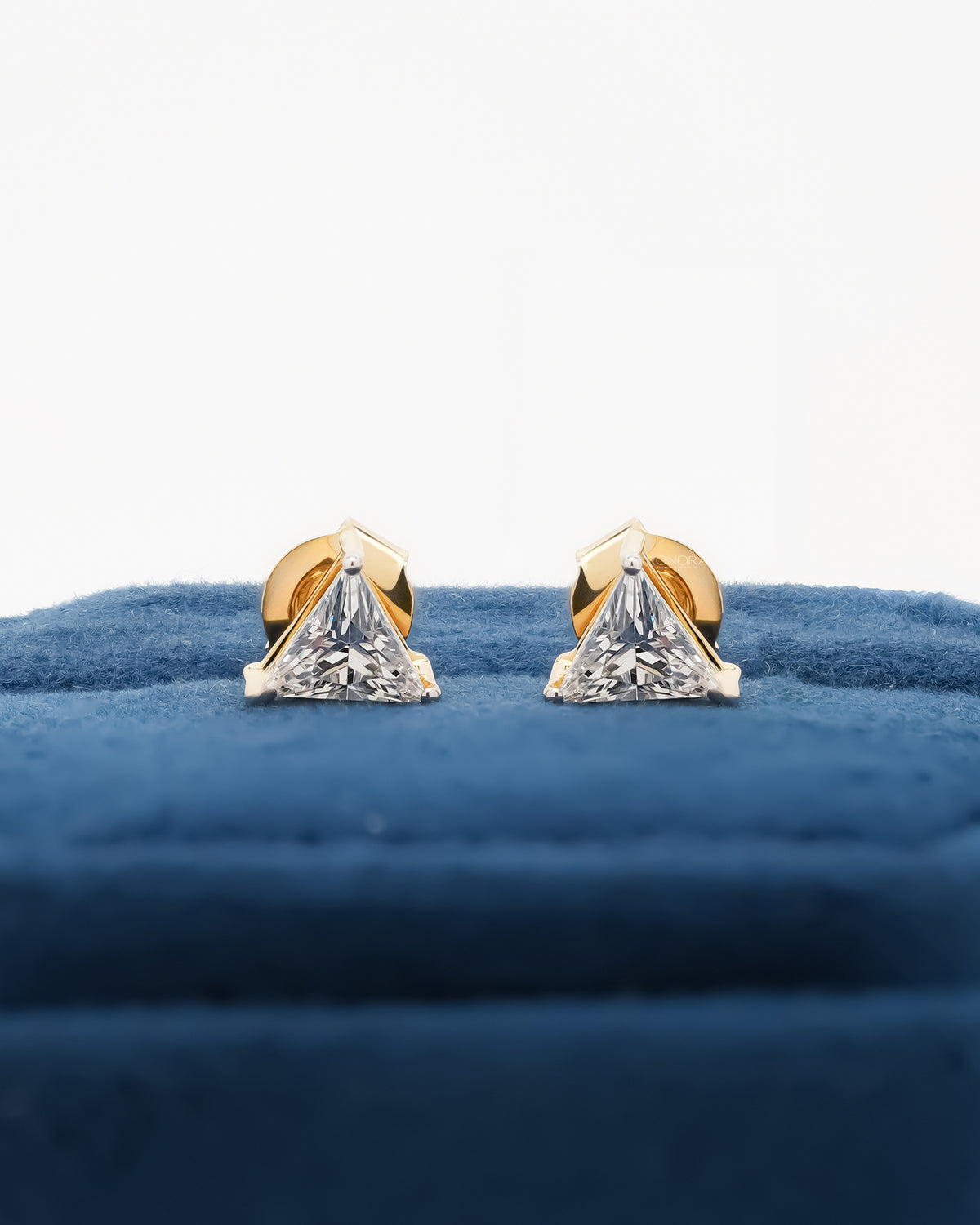 Pair of trillion cut lab grown diamond earrings in yellow gold standing on a blue velvet box
