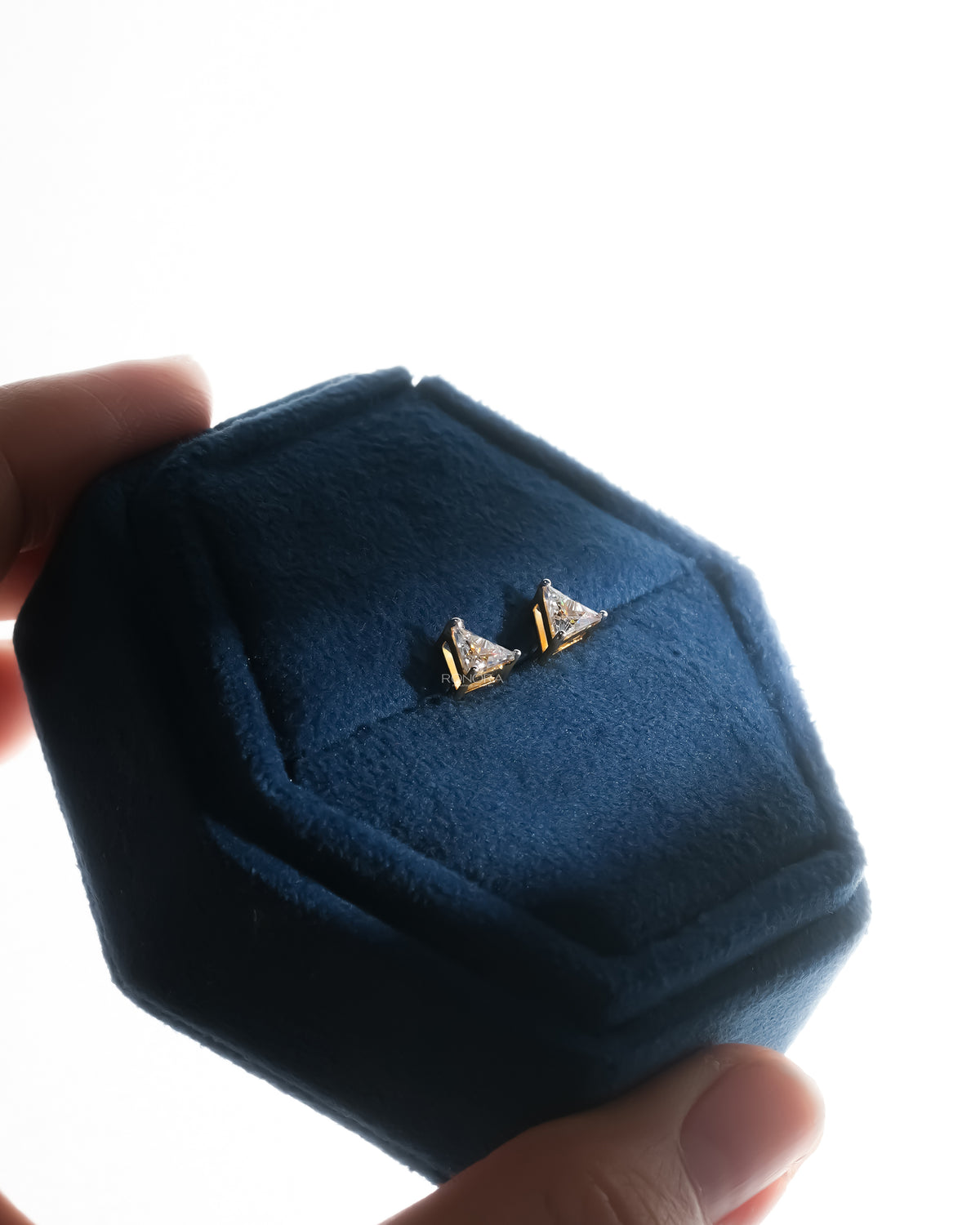 Trillion cut lab grown diamond earrings in yellow gold in a blue velvet jewelry box held in hand