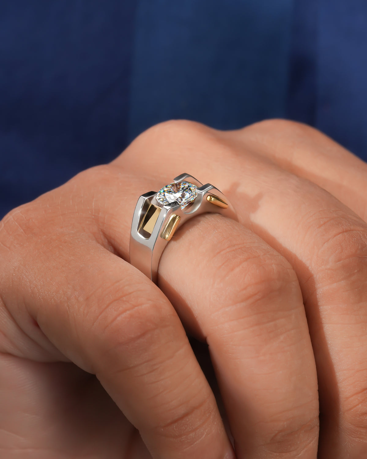 Side angle of a round lab grown diamond solitaire ring in two tone gold worn on a hand against a navy background