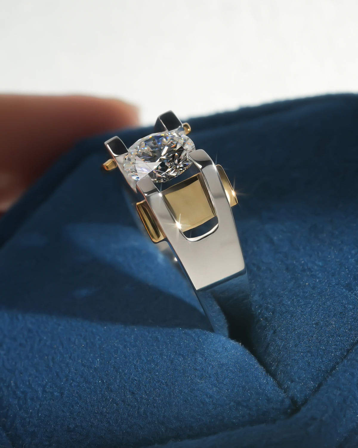 Angled close-up of a round lab grown diamond solitaire ring with white gold band and yellow gold accents on blue velvet