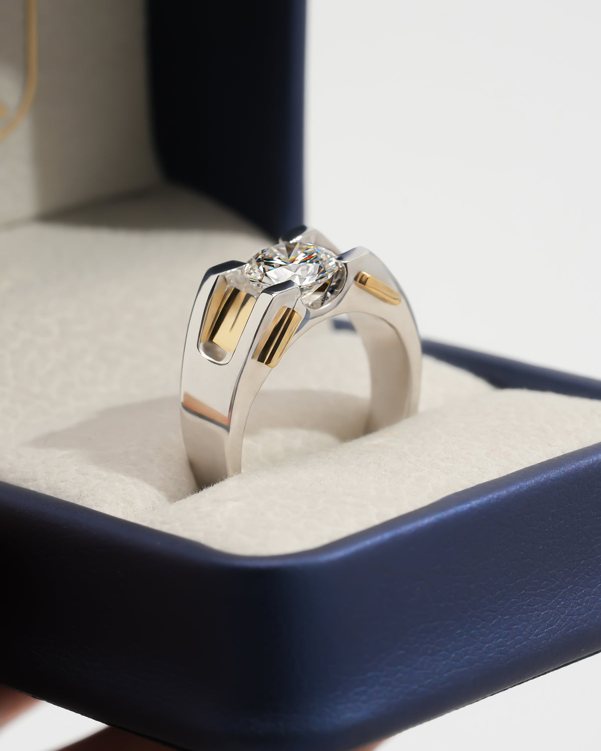 Angle view of a round lab grown diamond solitaire engagement ring in two tone gold, in an open navy ring box