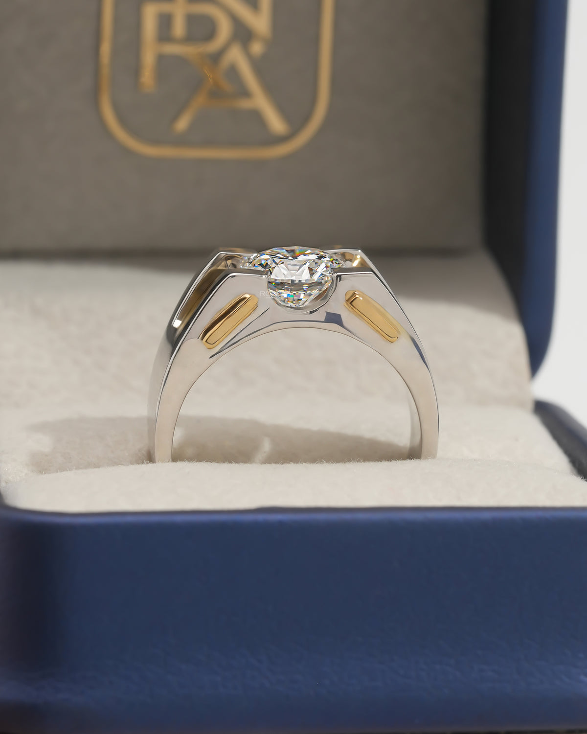 Back view of a round lab grown diamond solitaire ring in two tone gold standing in a navy and cream ring box