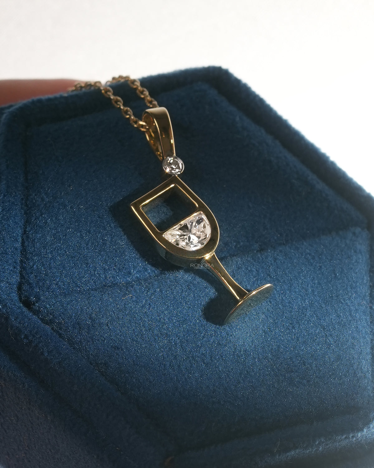 Wine glass lab grown diamond pendant in yellow gold on a dark blue velvet jewelry box, angled side view