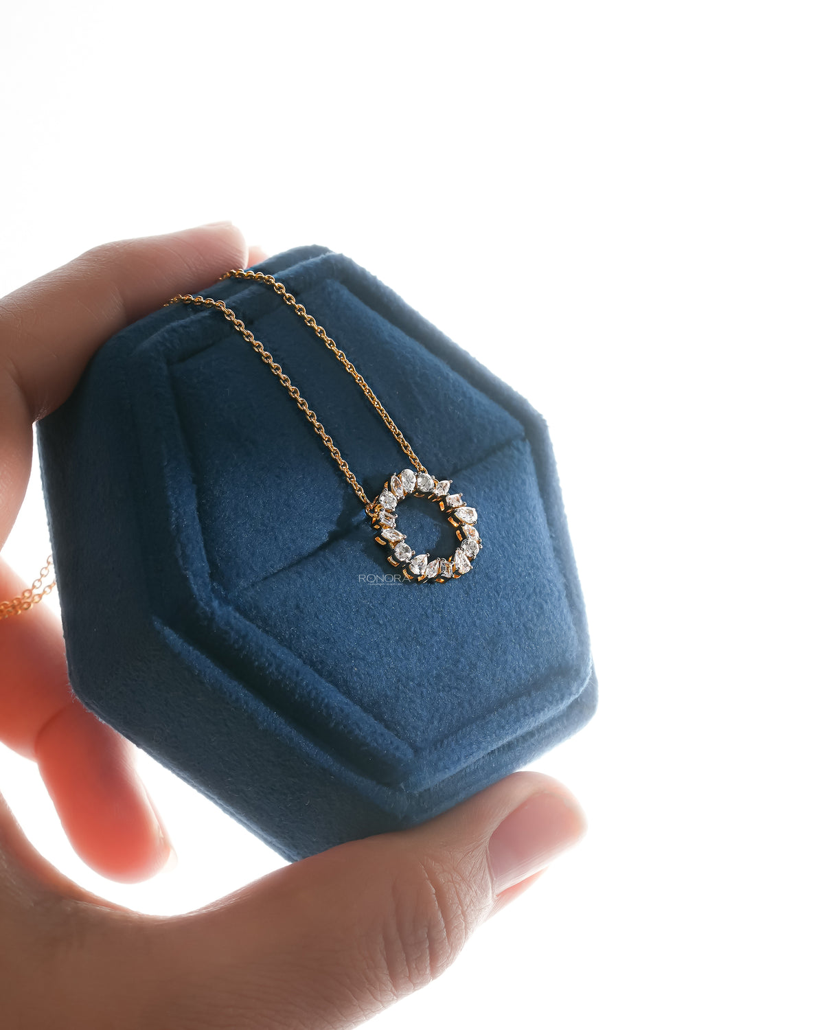 Angled view of a wreath lab grown diamond necklace in yellow gold hanging over a blue velvet jewelry box held in hand