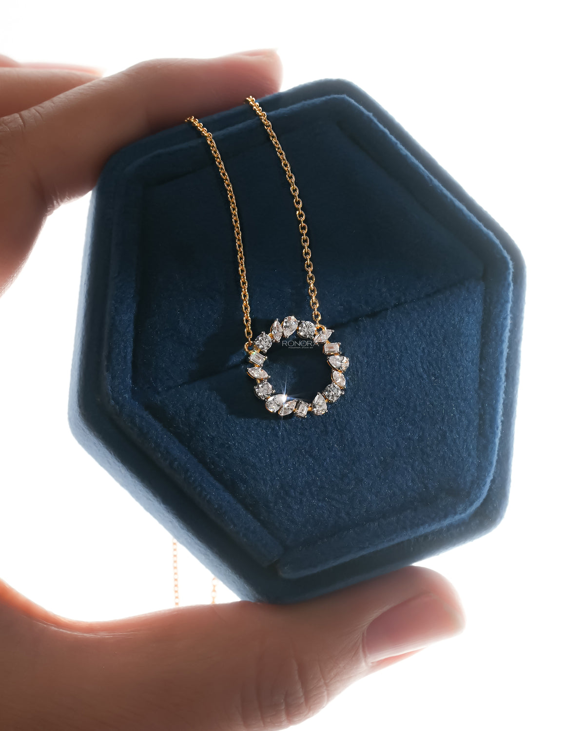 Sparkling wreath lab grown diamond necklace with an open circle pendant, yellow gold chain, backlit in a blue velvet box