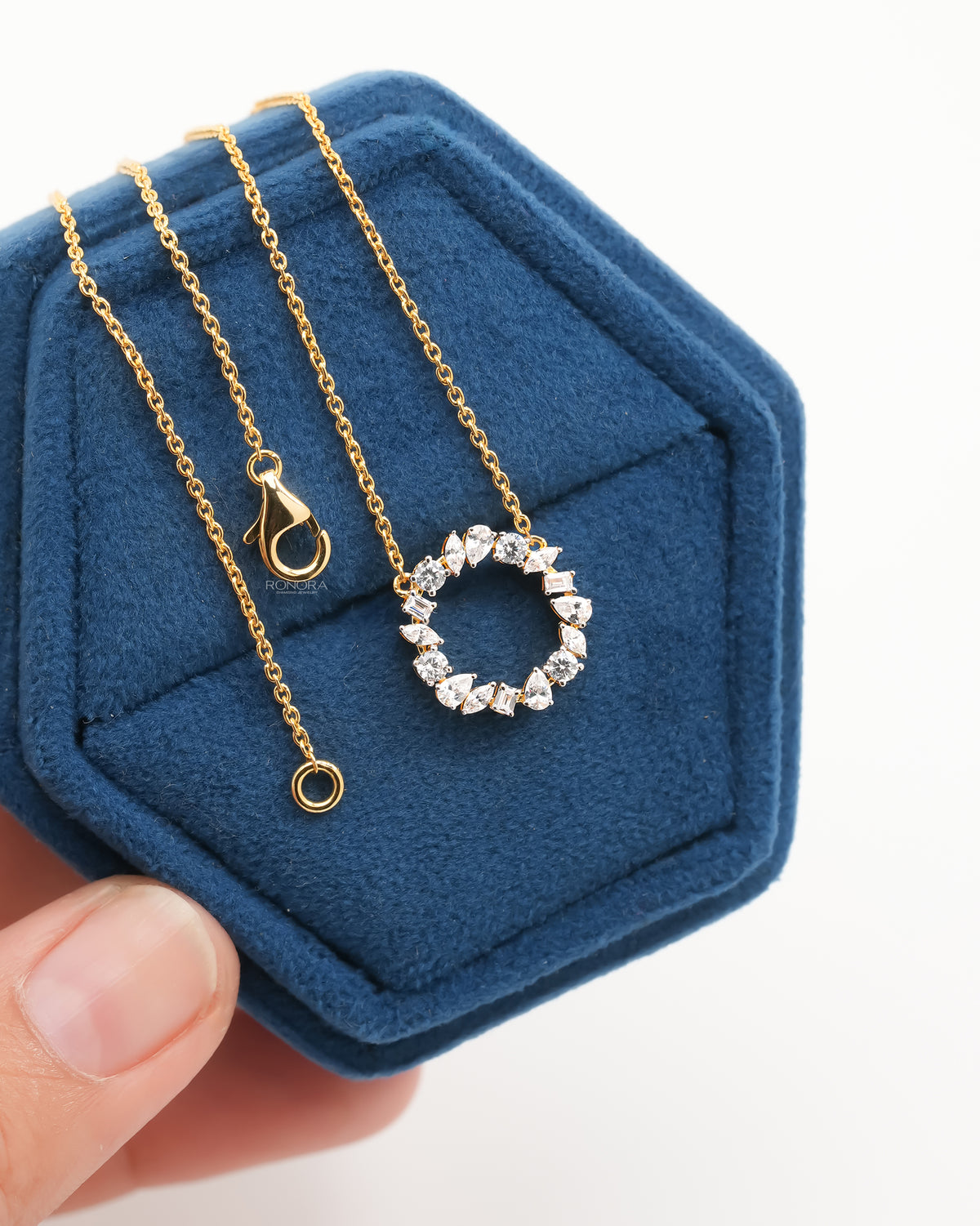 Wreath lab grown diamond necklace with yellow gold chain and clasp, resting in a blue velvet jewelry box held in hand