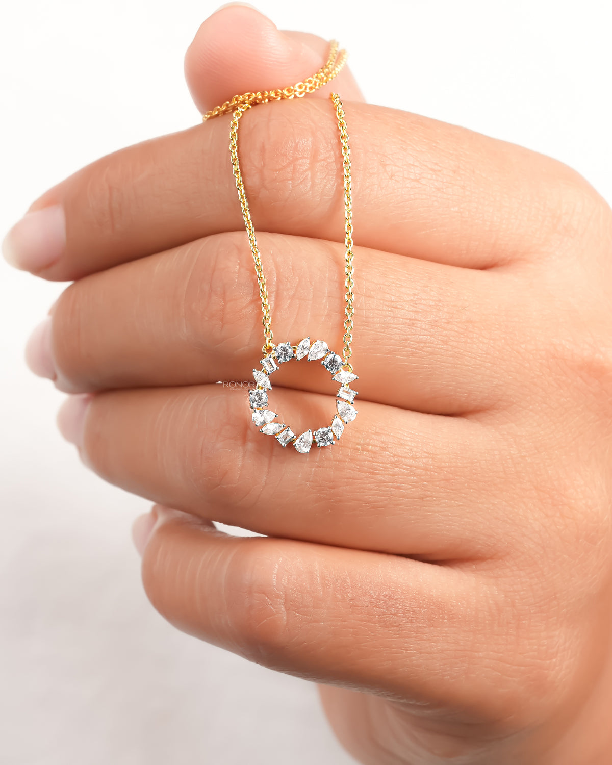 Hand holding a wreath lab grown diamond necklace, open circle pendant of mixed shape stones on a yellow gold chain