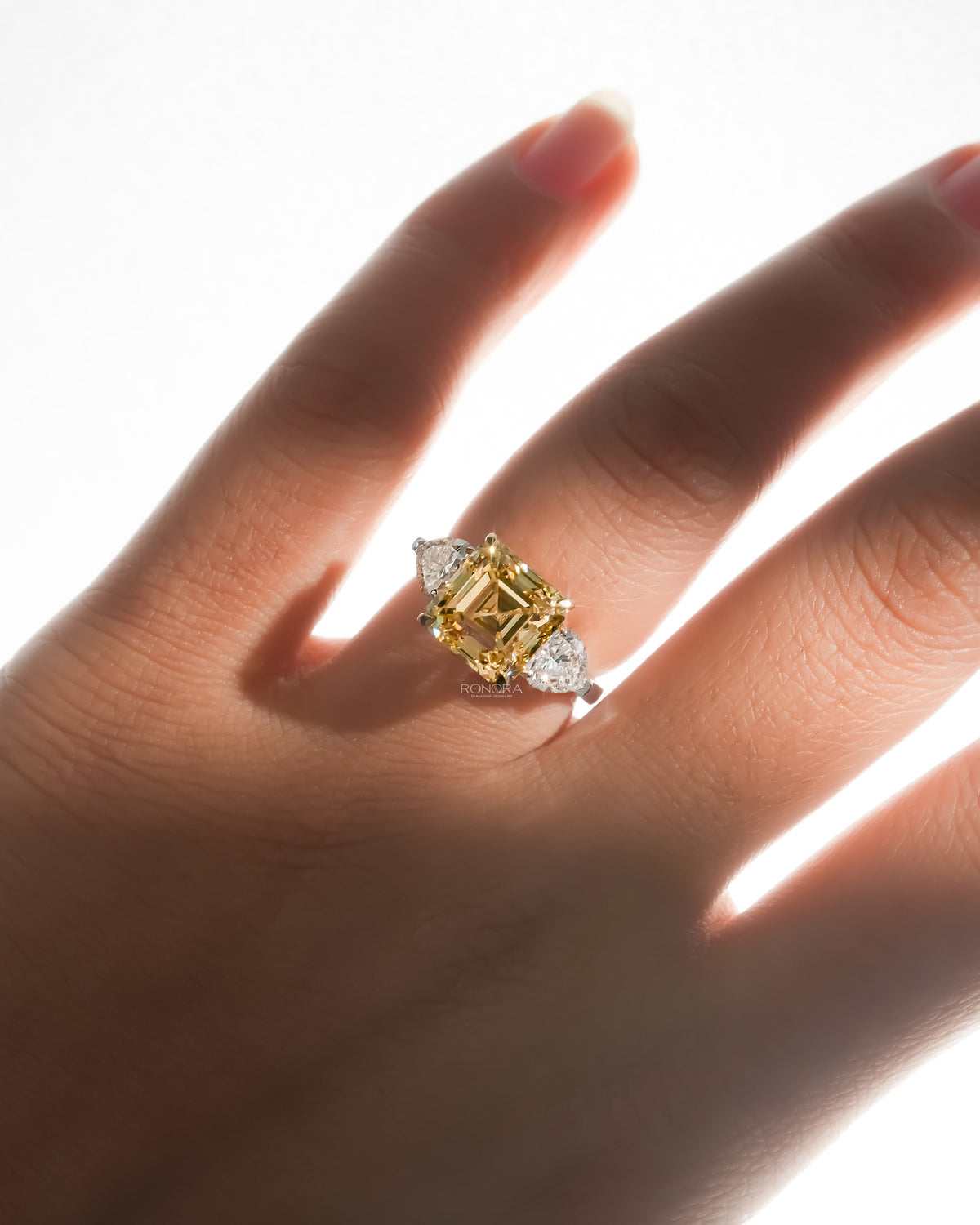 Asscher yellow lab grown diamond ring worn on a sunlit hand with white heart shaped side stones