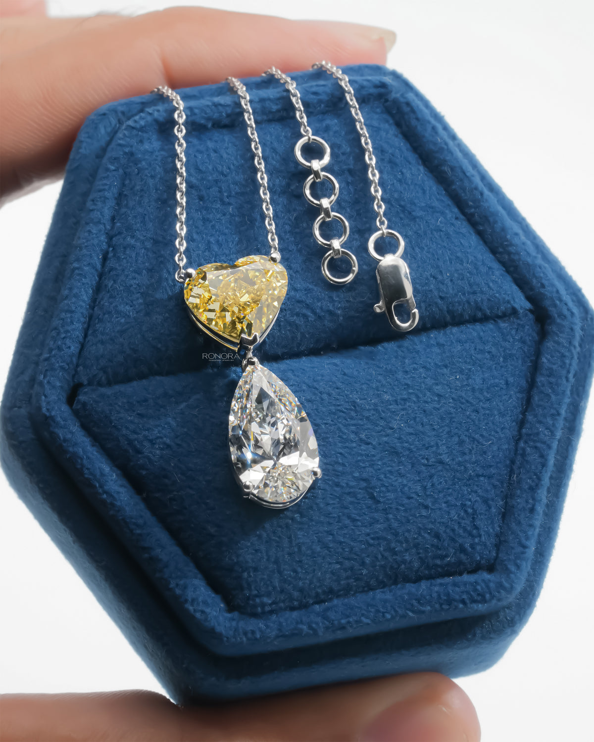 Yellow heart lab grown diamond necklace with white pear drop, chain extender and clasp shown on a blue velvet box
