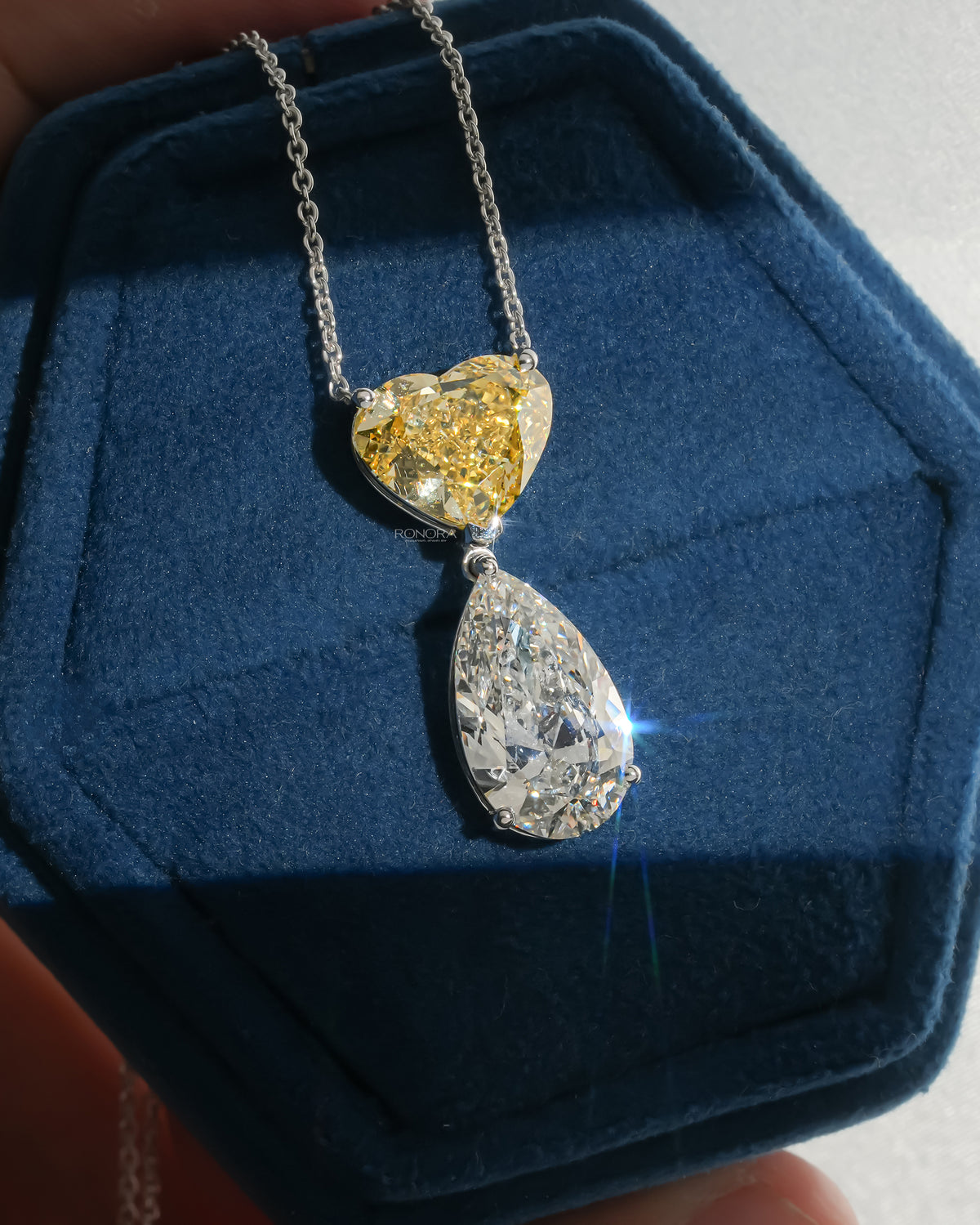 White gold necklace with a yellow heart lab grown diamond above a large white pear drop, on navy velvet