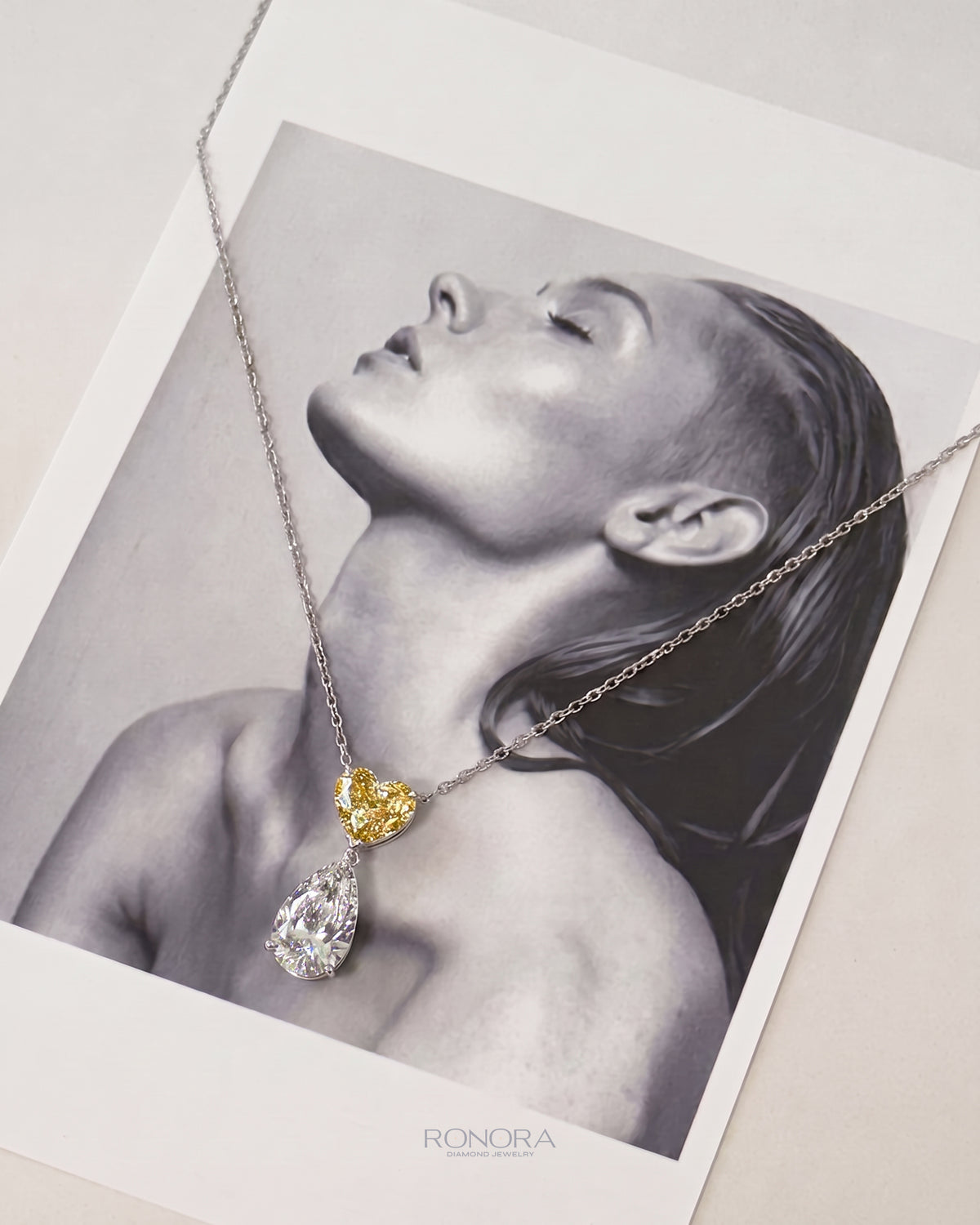 Yellow heart lab grown diamond necklace with a white pear drop, laid over a black and white portrait print