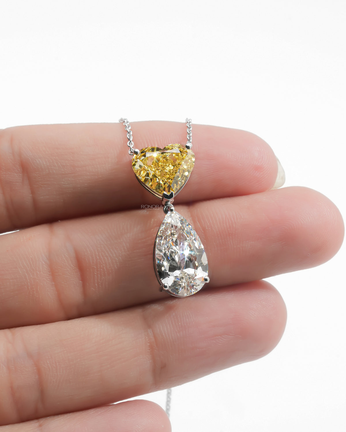 Yellow heart lab grown diamond necklace with a white pear drop resting across a hand, on a white gold chain