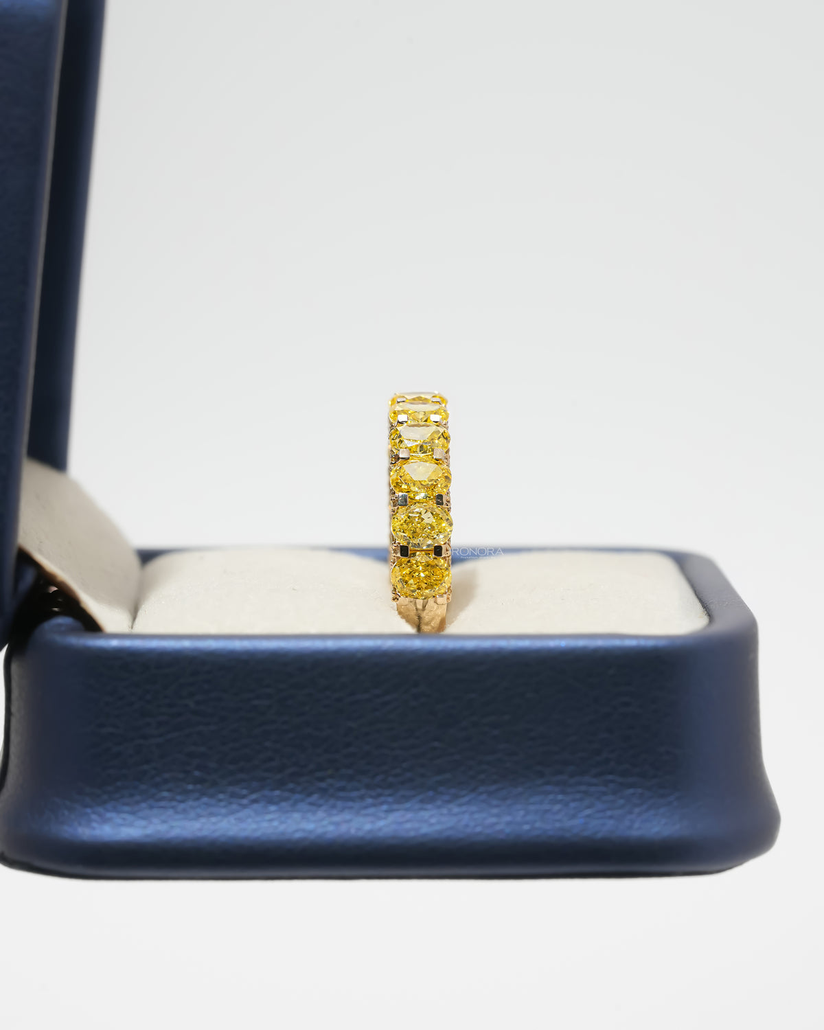 Side view of a yellow lab grown diamond oval eternity band standing upright in a navy blue ring box