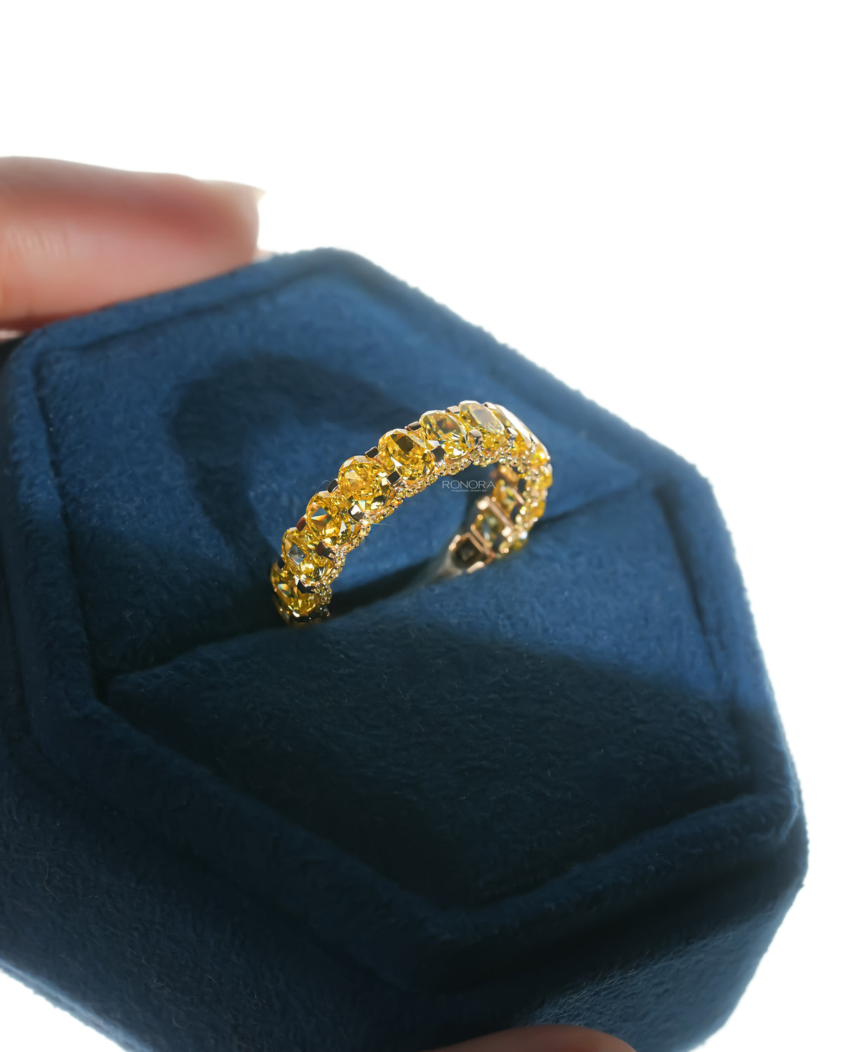 Angled view of a yellow lab grown diamond oval eternity band in a blue velvet ring box, showing the row of oval stones