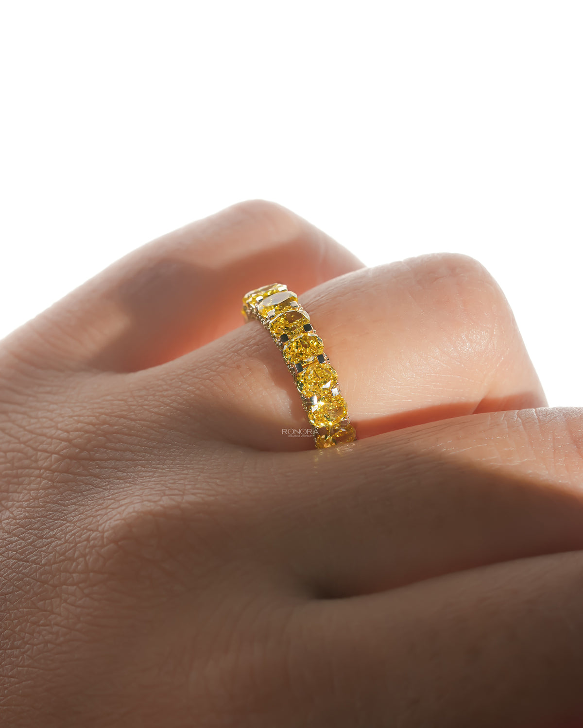 Close-up of a yellow lab grown diamond oval eternity band on a finger, prong set yellow oval stones along the band