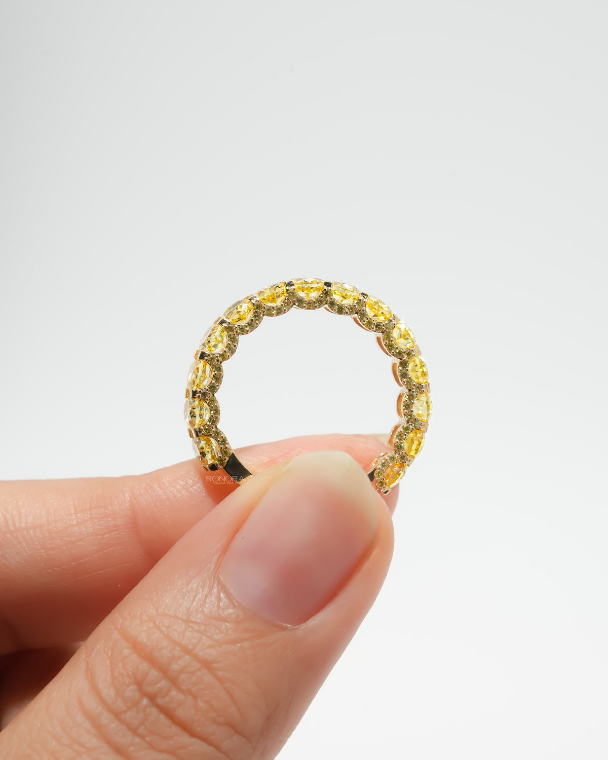 Yellow lab grown diamond oval eternity band held between fingertips, showing the full circle of yellow oval stones