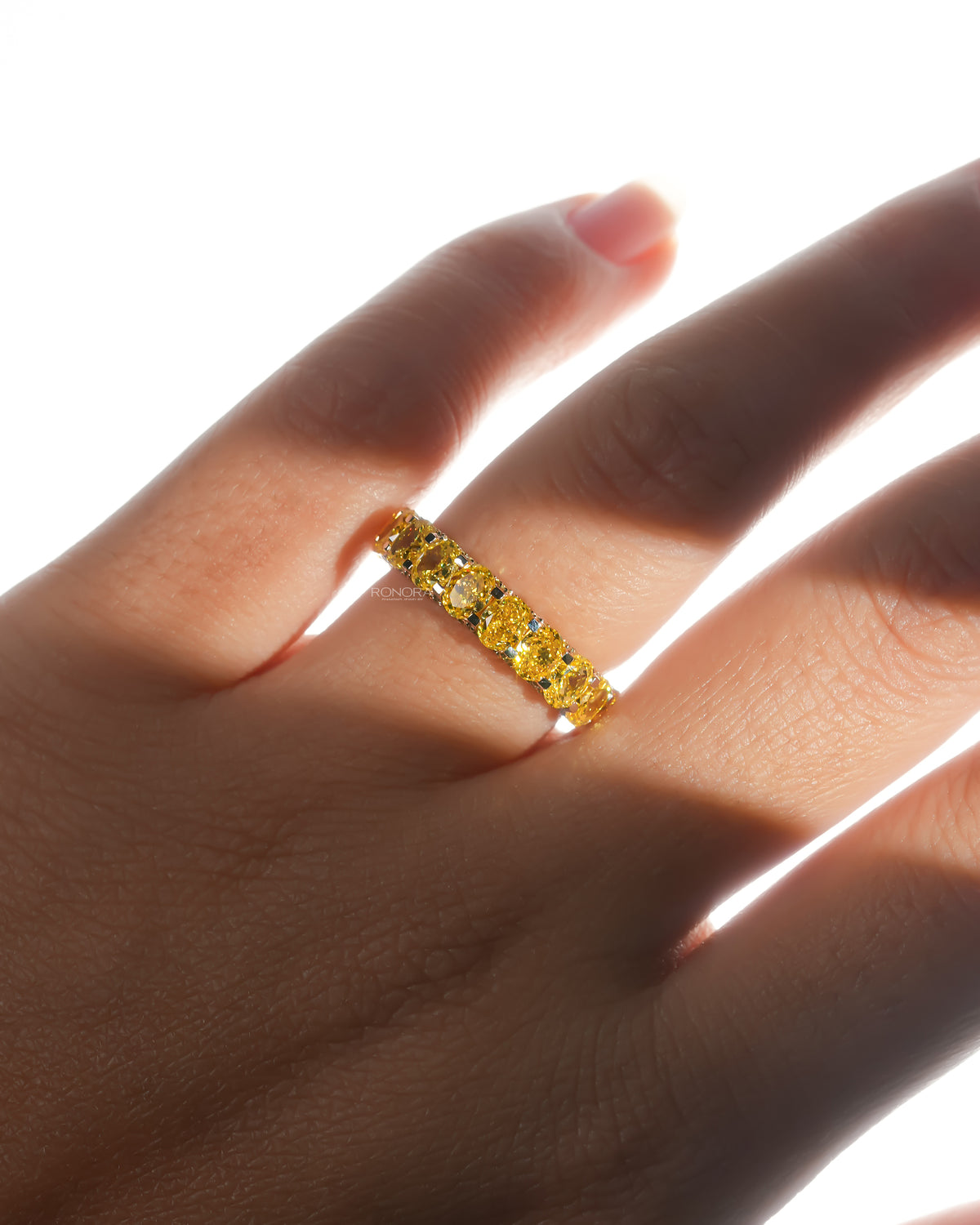 Hand wearing a yellow lab grown diamond oval eternity band in soft sunlight, with a row of yellow oval stones