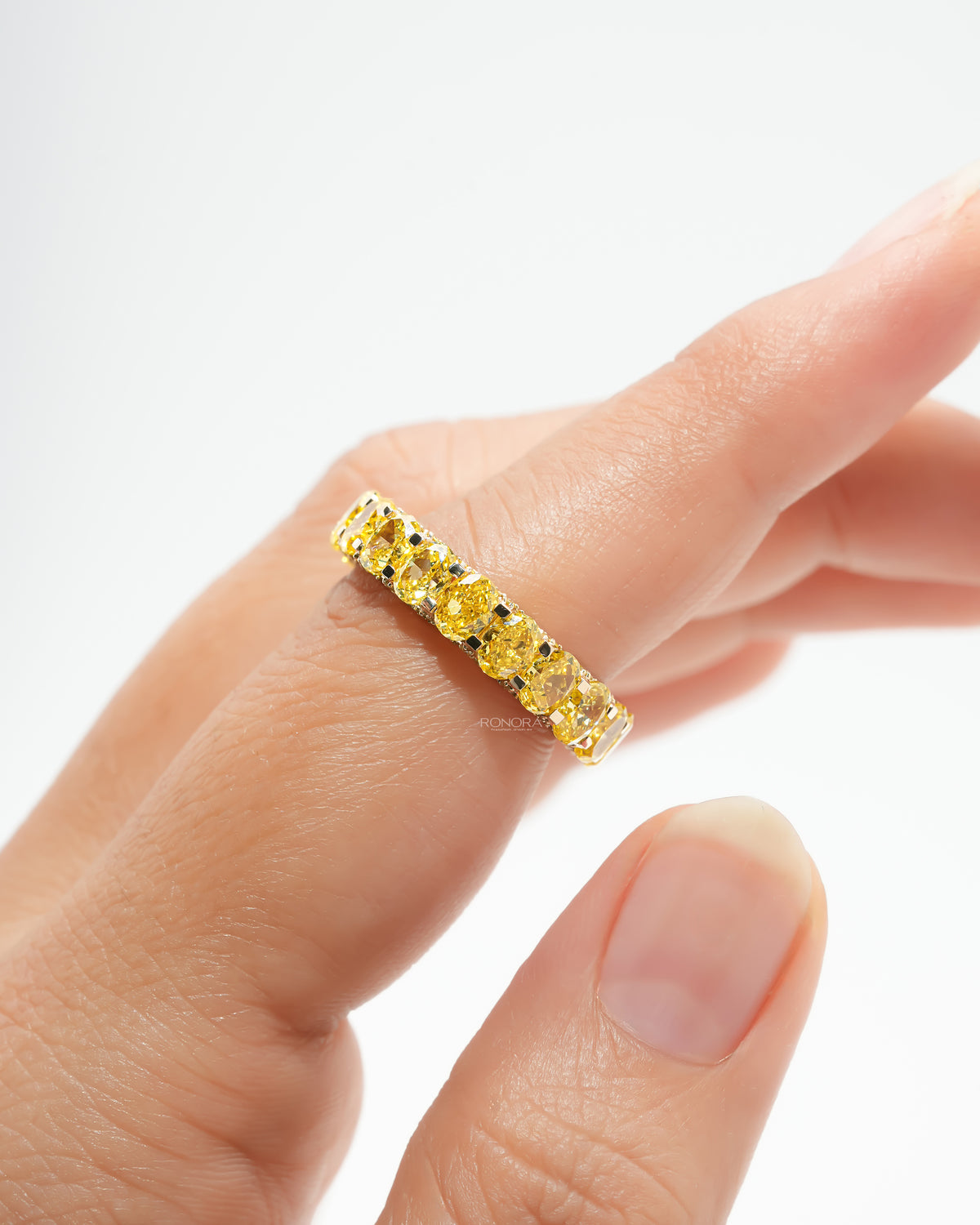Yellow lab grown diamond oval eternity band worn on a finger, close view of the row of bright yellow oval stones