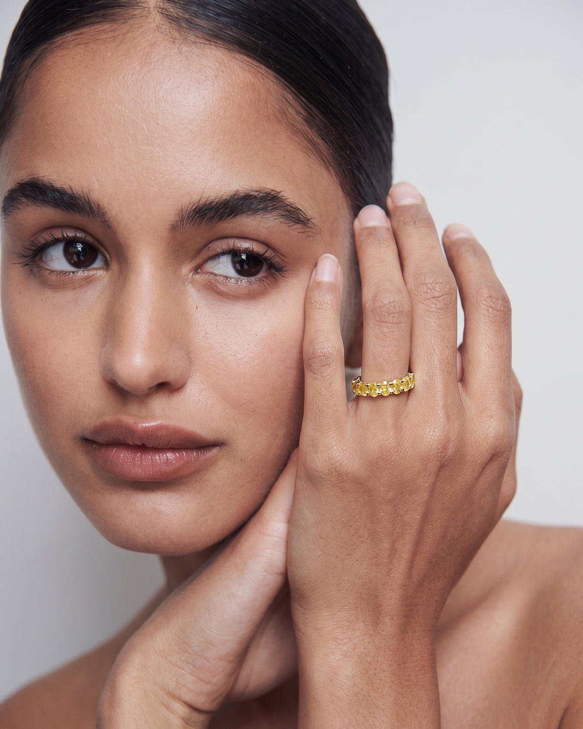 Model touching her face and wearing a yellow lab grown diamond oval eternity band in yellow gold on her ring finger