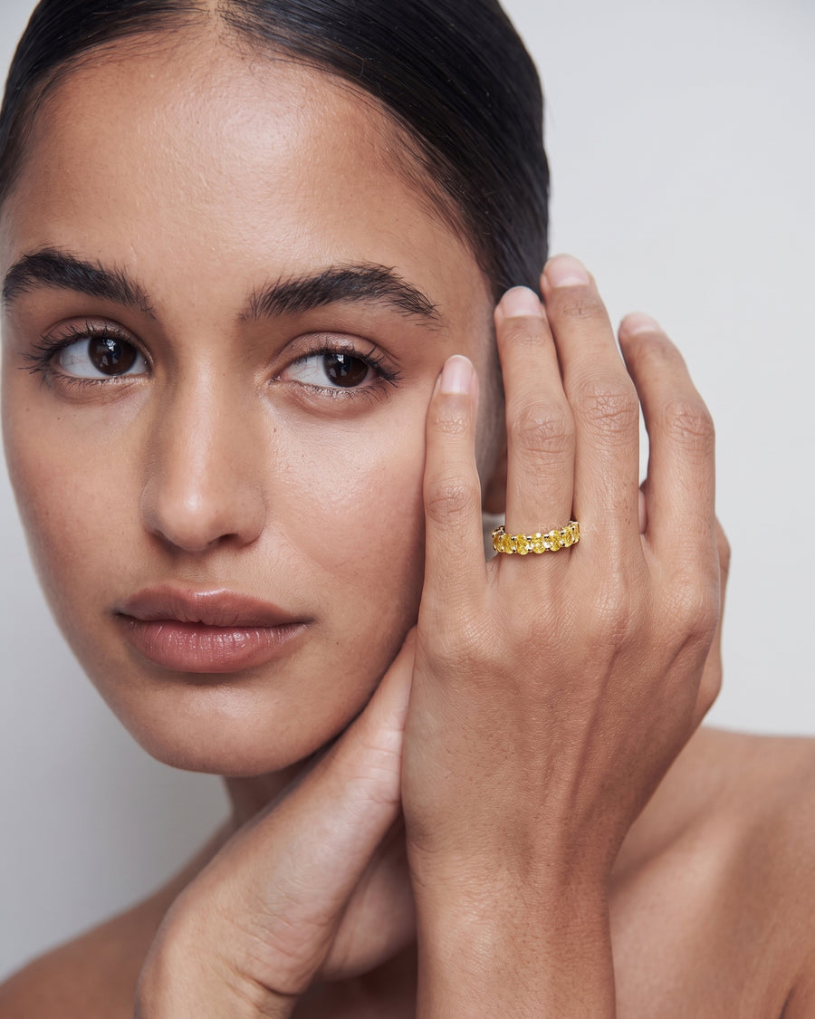 Model touching her face and wearing a yellow lab grown diamond oval eternity band in yellow gold on her ring finger