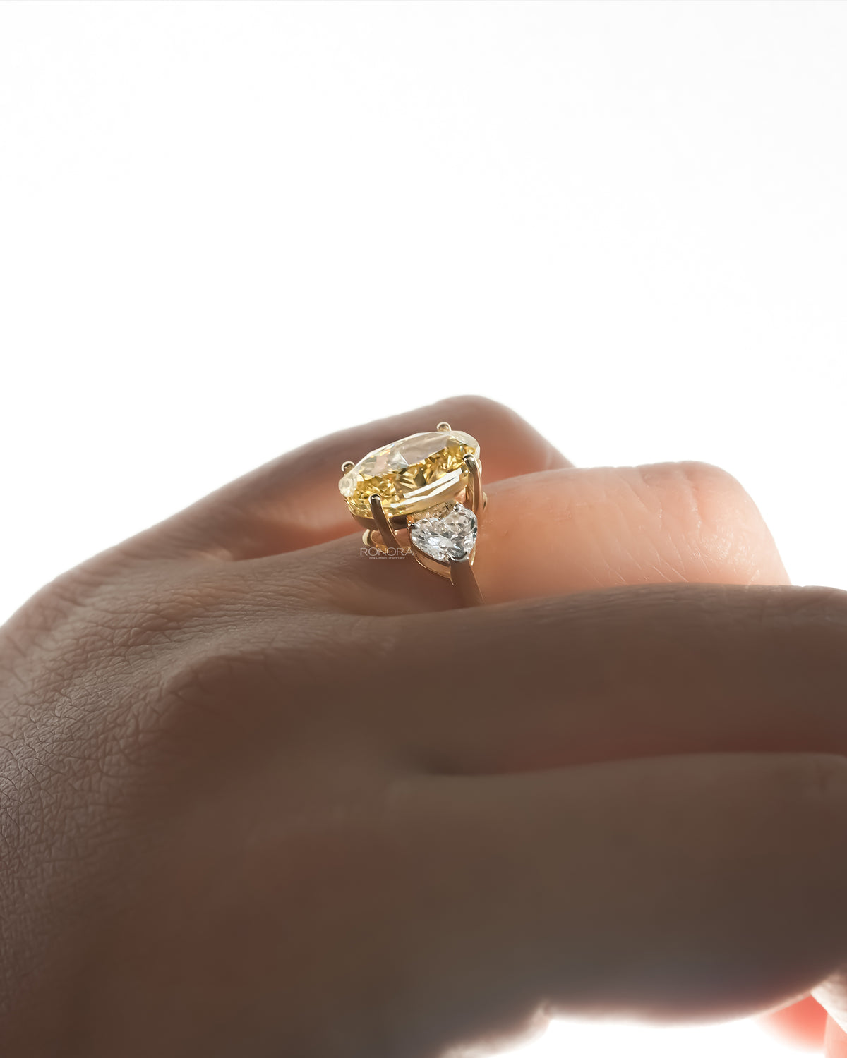 Side view of an oval yellow lab grown diamond ring on a finger, yellow gold prongs and a heart shaped side stone