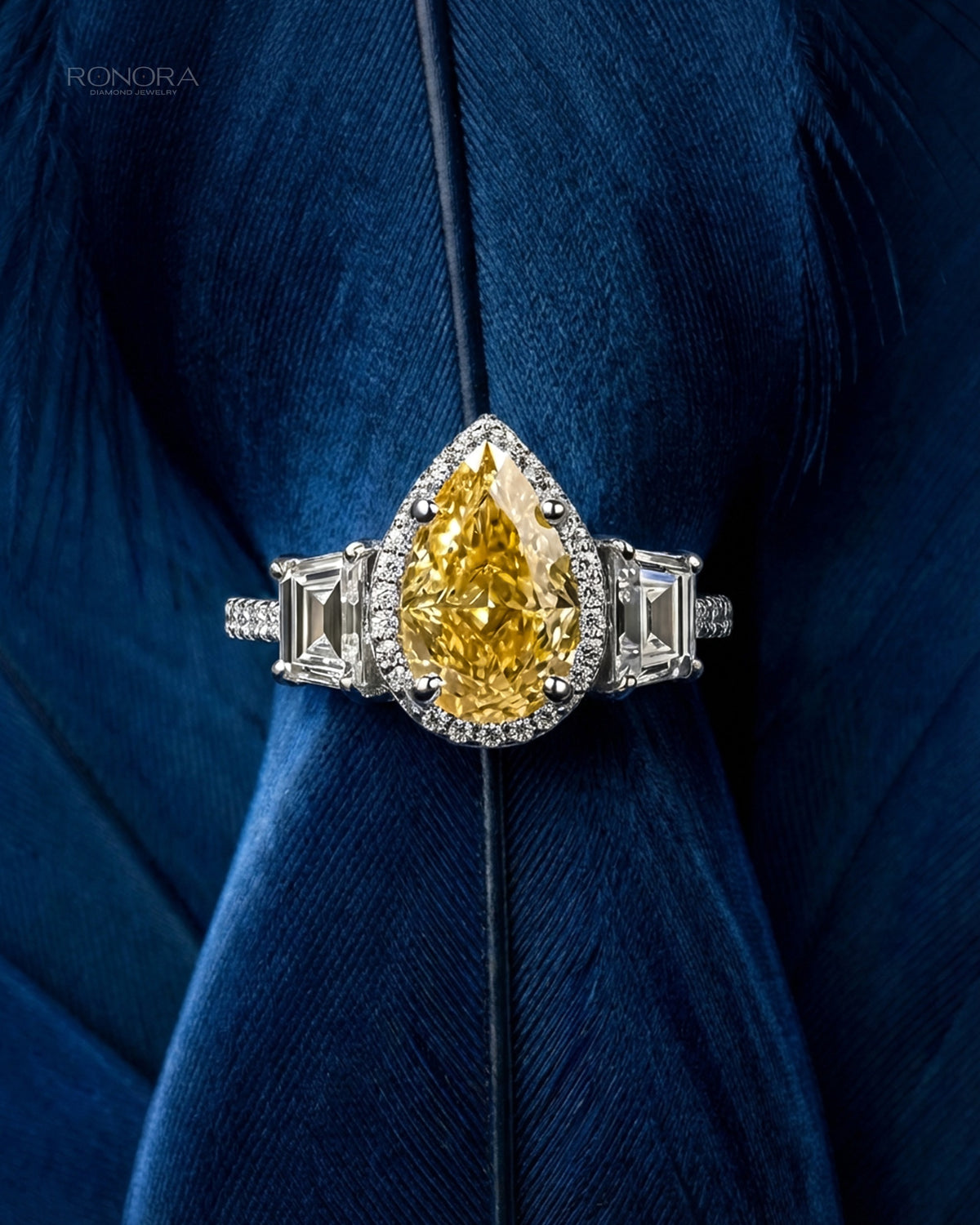 Yellow pear lab grown diamond baguette halo ring in white gold with step cut side stones, styled on a deep blue feather
