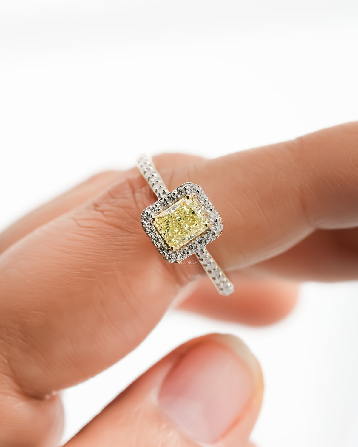 Fancy yellow lab grown diamond halo ring held between fingers showing the pave halo