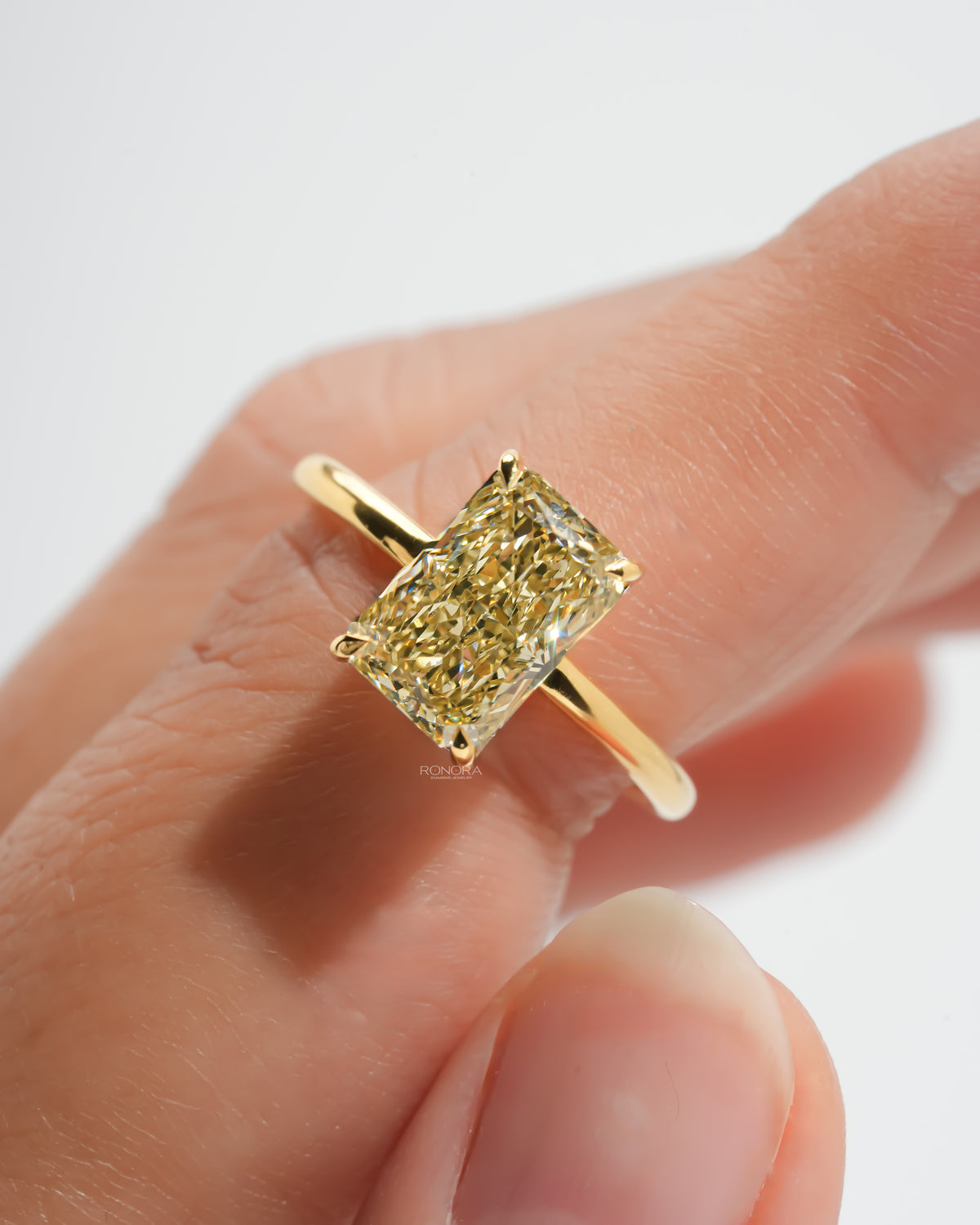 Close-up of a yellow radiant lab grown diamond solitaire ring in yellow gold on a fingertip