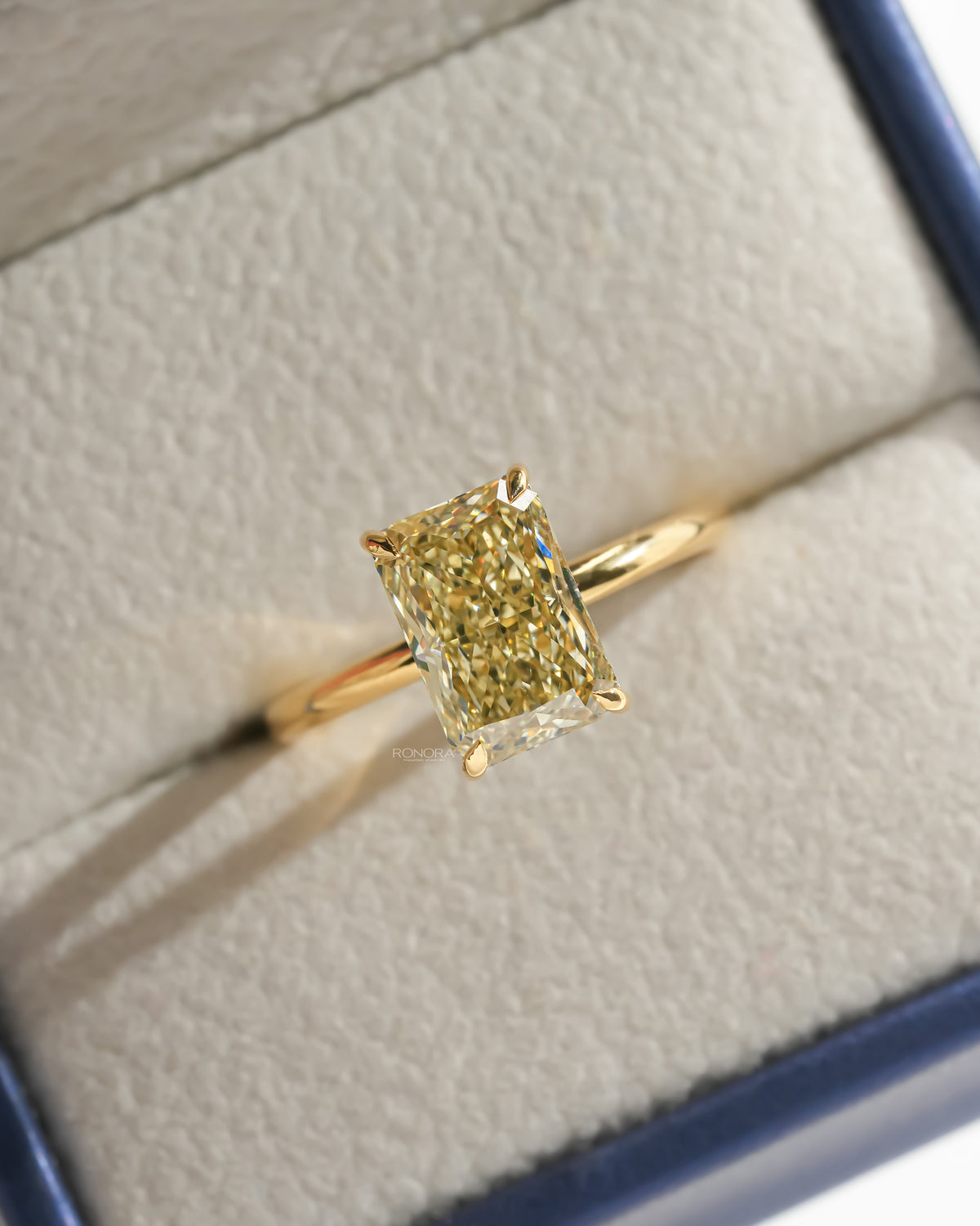 Yellow radiant lab grown diamond solitaire ring in yellow gold resting in a cream and navy ring box, top view