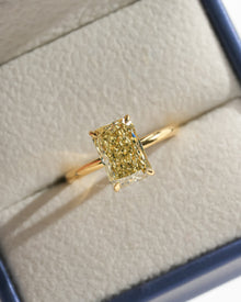 Yellow radiant lab grown diamond solitaire ring in yellow gold resting in a cream and navy ring box, top view
