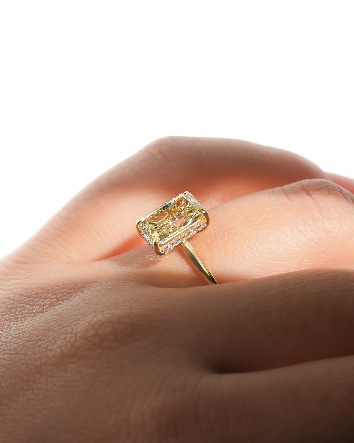 Side angle of a yellow radiant lab grown diamond solitaire ring with a hidden halo worn on a hand, yellow gold