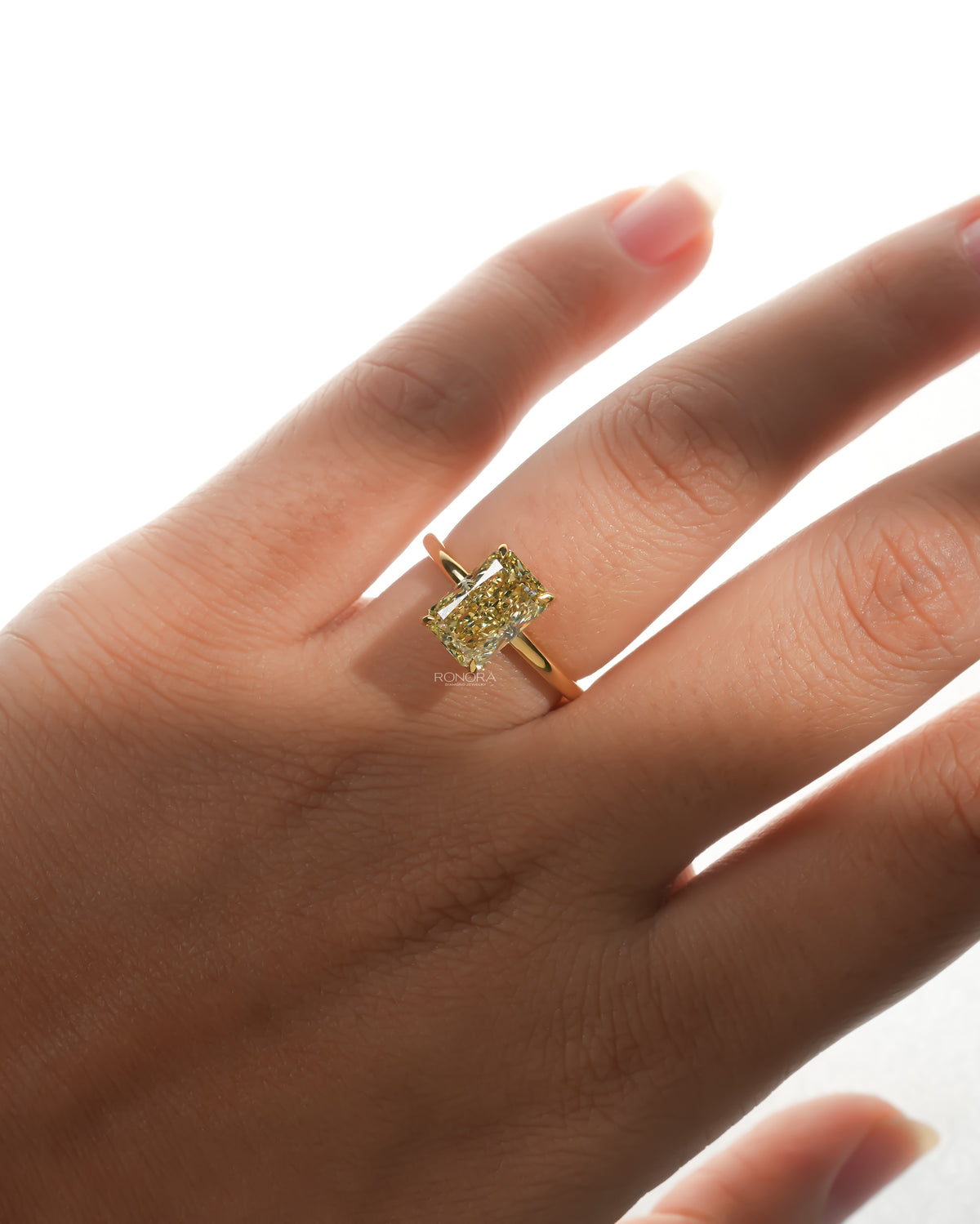 Hand wearing a yellow radiant lab grown diamond solitaire ring with a thin yellow gold band, front view