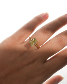 Hand wearing a yellow radiant lab grown diamond solitaire ring with a thin yellow gold band, front view